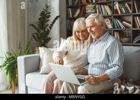 Im Alter von Mann und Frau zusammen zu Hause im Wohnzimmer sitzen mit Laptop auf den Bildschirm zeigen lächelnd Stockfoto