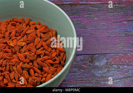 Keramische Schüssel voller trockenen Goji Beeren auf alten hölzernen Hintergrund im Vintage Style. Schließen, flache, horizontale Ansicht von oben. Stockfoto