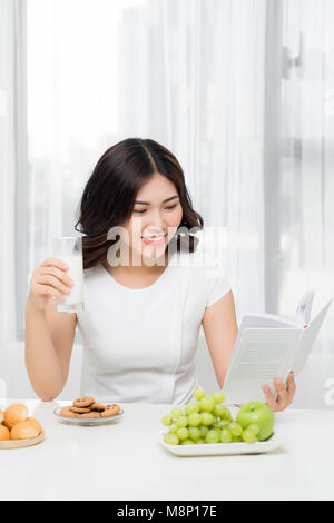 Lächelnde Frau mit einer entspannenden gesundes Frühstück zu Hause sitzen am Küchentisch, sie ist lesen Buch Stockfoto