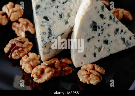 Keile weicher Blauschimmelkäse mit Walnüssen auf schwarzem Teller. Stockfoto