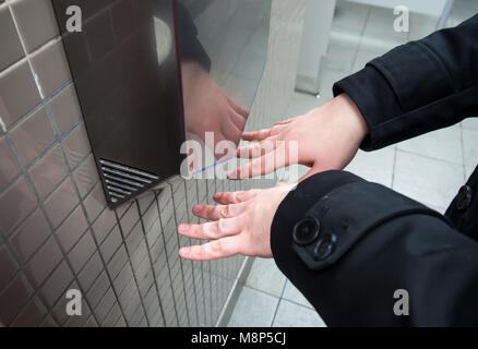 Man trocknet nasse Hände mit einem elektrischen Händetrockner Stockfoto