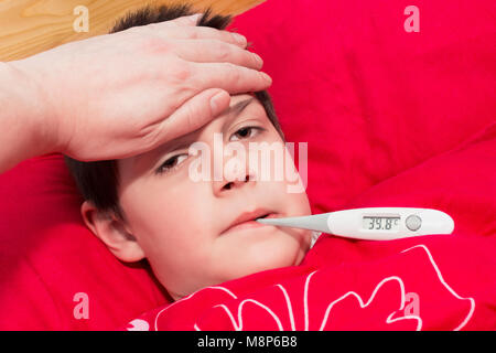 Ein kranker Junge im Bett lag, mit einem Thermometer in den Mund. Kalte Kompresse auf die Stirn des Kindes. Grippeepidemie in der Tschechischen Republik. Stockfoto