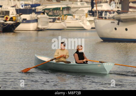 Mann und eine Frau in einem Ruderboot aus Gießen mit Ruder in der Hand in Falmouth Harbour Boote Stockfoto