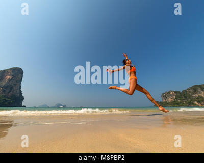 Unbeschwerte Frau im Bikini am Strand springen Stockfoto