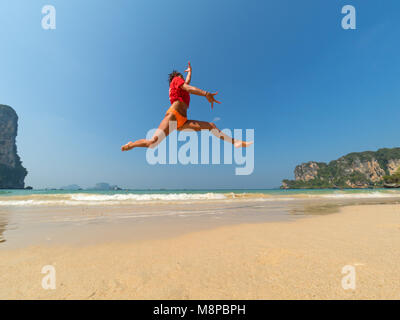 Unbeschwerte Frau im Bikini am Strand springen Stockfoto