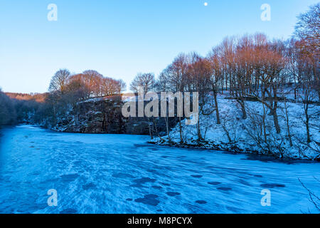 Gefrorenes Wasser in den Gewässern des Anglezarke Behälter Chorley Lancashire Großbritannien als die Sonne untergeht und der Mond erscheint in den blauen Himmel über Stockfoto