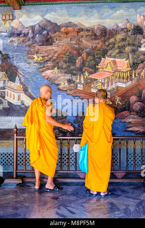 Zwei buddhistische Mönche in gelbe Umhänge sind mit einem großen Gemälde im Grand Palace Stockfoto