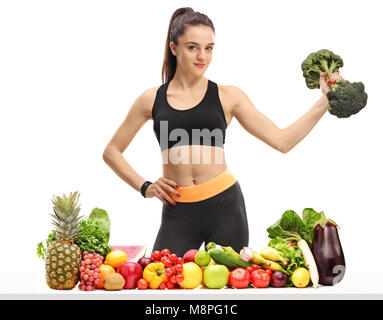 Fitness Frau mit Brokkoli Hantel hinter einem Tisch mit Obst und Gemüse auf weißem Hintergrund Stockfoto