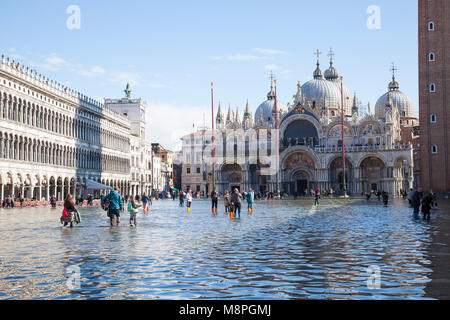 Touristen zu Fuß durch die Acqua Alta High Tide mit Koffer, Markusplatz, Piazza San Marco, Venedig, Venetien, Italien vor St Marks Basilikum