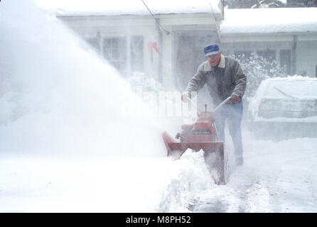 Ein Mann mit einer Schneefräse in seiner Einfahrt während eines Schneesturmes. USA Stockfoto