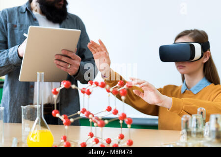 Junge Lehrerin mit Virtual Reality Brillen und einem 3D-Präsentation Schüler im Chemieunterricht zu unterrichten. Bildung, VR, Nachhilfe, Neue Technologien. Stockfoto