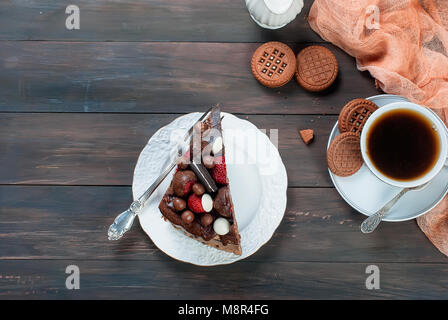 Stück Schokolade Kuchen auf weissen Teller, Tasse schwarzen Kaffee, Kanne und Schokolade Cookies auf dunklen Holztisch Hintergrund. Sicht von oben mit Kopie spa Stockfoto