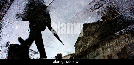 Unscharf man walking city street mit gefalteten Dach kurz nach dem Regen, der Reflexion Silhouette in der Pfütze Stockfoto