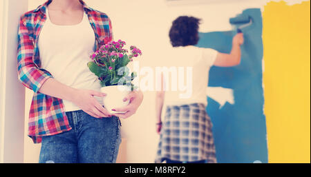 Glückliches Paar Haupterneuerungen zu tun, ist der Mann das Zimmer und die Frau halten den Topf mit Blumen Malerei. Stockfoto