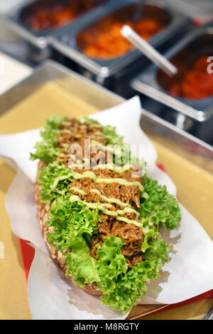 Köstliche zog pork Sandwich mit Geschredderten würzigen Fleisch beträufelt mit einem Dressing auf einem Bett von Salat auf das verfügbare Papier serviert in einem Fast Food Restaurant, Bar Stockfoto