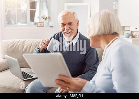 Angenehme älterer Mann lesen Artikel seiner Frau, die ihn Stockfoto