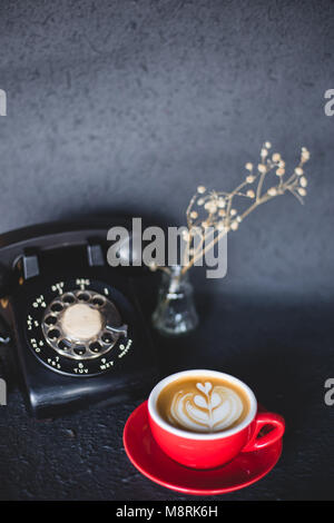 Latte Art Kaffee mit retro Telefon auf schwarz Farbraum Stockfoto