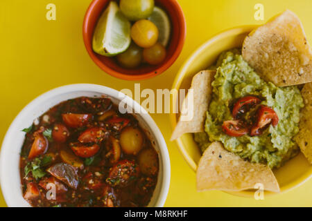 Ansicht von oben von Salsa und Guacamole serviert mit Zutaten auf gelbem Hintergrund Stockfoto