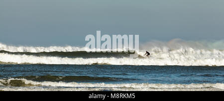 Panorama-aufnahme eines einsamen Surfer, racing in Küste im Atlantischen Ozean (Keltische See), Bude, Cornwall, Großbritannien Stockfoto