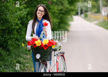 Portrait von fröhliche junge Frau mit Fahrrad holding Tulip auf der Straße Stockfoto