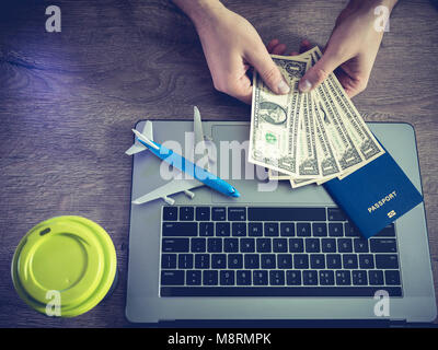 Die Hände des Mannes betrachten, Banknoten, die von einem Dollar, vor dem Hintergrund von einer Tasse Kaffee der Laptop, der Pass und das Flugzeug. Stockfoto