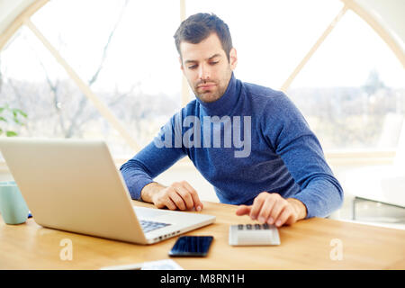 Junge buisnessman am Schreibtisch sitzen und mit Hilfe der Rechner und Laptop während der Arbeit am neuen Projekt. Home Office. Stockfoto