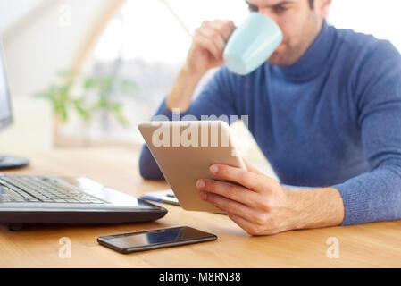 Hohen Winkel cropeed erschossen der junge Unternehmer sitzen am Schreibtisch vor, während mit digitalen Tablet- und trinken eine Tasse Kaffee. Stockfoto