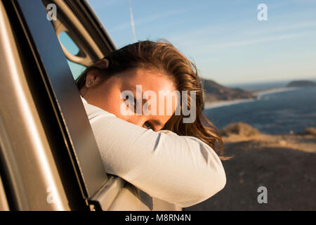 Portrait von Frau suchen durch Auto Fenster am Strand gegen Himmel bei Sonnenuntergang Stockfoto