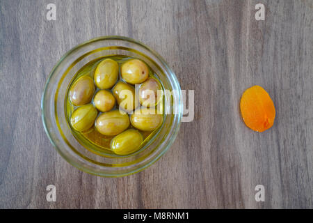 Nur grüne Oliven in eine Glasschüssel und getrocknete Aprikosen auf einem brawn Tisch für Frühstück Stockfoto