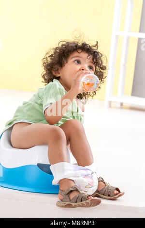 Kleines Baby, sitzt auf einem blauen Topf und Getränke Wasser aus einer Flasche innen Hintergrund Stockfoto