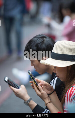 Zwei junge Erwachsene mit Handys auf den Straßen von Shanghai in China. Stockfoto