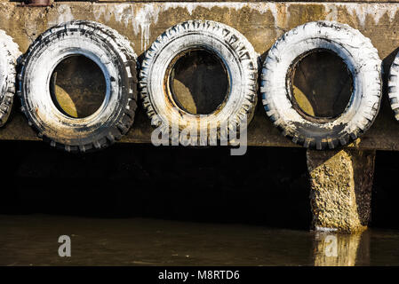 Drei weisse und verwitterten Autoreifen auf der Seite von einem Betonpfeiler in einem Hafen. Stockfoto