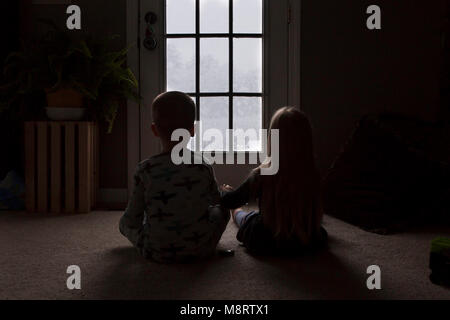 Ansicht der Rückseite des Geschwister auf der Suche durch das Fenster beim Sitzen auf dem Boden in der Dunkelkammer Stockfoto