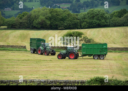 Arbeiten im landwirtschaftlichen Bereich, 2 grüne Fendt Traktoren sind das Ziehen von Anhängern - 1 ist geladen mit geschnittenem Gras für Silage und 1 ist leer - West Yorkshire, England, Großbritannien Stockfoto
