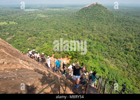 Ein Blick auf die Touristen klettern auf den Gipfel des Sigiriya Felsen, die Aussicht und wie steil an einem sonnigen Tag mit blauen Himmel. Stockfoto