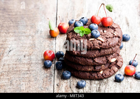 Stapel von dunkler Schokolade Cookies mit frischen Heidelbeeren und wilde Äpfel auf Holztisch, isoliert Stockfoto