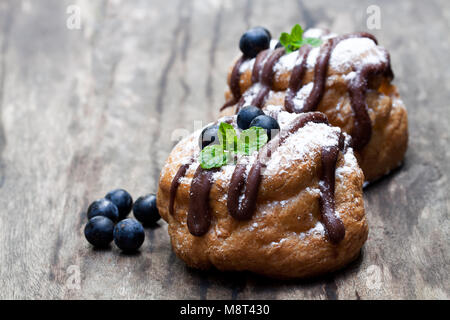 Die belgische Schokolade choux Brötchen gefüllt mit Heidelbeeren und Creme auf hölzernen Tisch Stockfoto