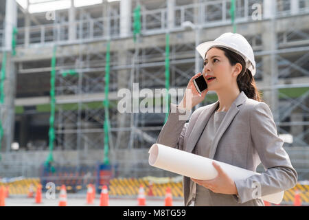 Weibliche Architekt, am Telefon zu sprechen. Eine Hand, die den Bau einer Blaupause. Stockfoto