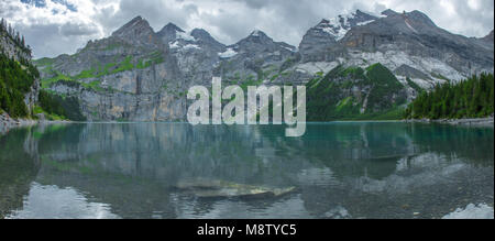 Fantastischer Panoramablick der Oeschinensee, alpine Tarn, Schweizer Alpen. Emerald Lake, tief blauen Wasser, noch Oberfläche. Wald, schroffe Berge und Gletscher Stockfoto