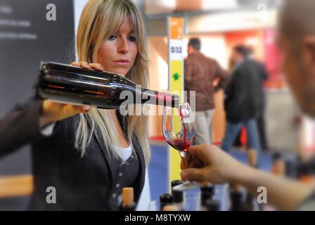 Blonde Frau gießen Rotwein aus der Flasche in das Glas des Kunden in Wein internationale Messe selektiven Fokus Effekt Turin Italien ca. November 20. Stockfoto