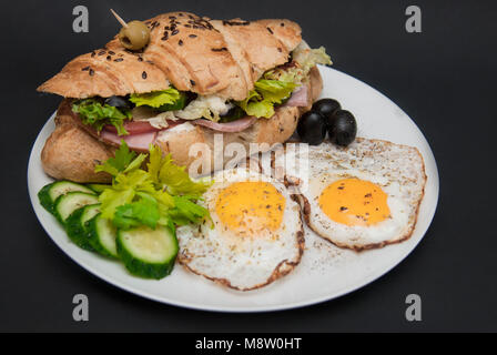 Frühstück auf weiße Platte mit Spiegelei und Croissant mit frischem Gemüse über schwarzen Hintergrund. Essen Konzept Stockfoto