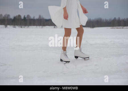 Füße der Frau in weißem Kleid und Schlittschuhen auf Schnee im Freien im Winter Stockfoto