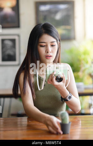 Gerne asiatische Frau unter Foto Kaktus von Vintage Kamera im Cafe, Lifestyle Konzept Stockfoto