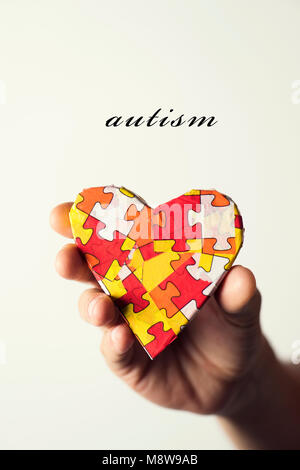 Das Wort Autismus und ein Herz mit vielen Puzzleteilen in verschiedenen Farben, Symbol der autism Bewußtsein, in der Hand des jungen kaukasischen ma gemusterten Stockfoto