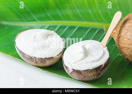 Köstliche vegane Kokos-eis in Schalen mit Holzlöffel auf Große grüne Palme Blatt auf weißem Marmor Tisch. Auf Basis pflanzlicher Ernährung gesundes Dessert Sup Stockfoto