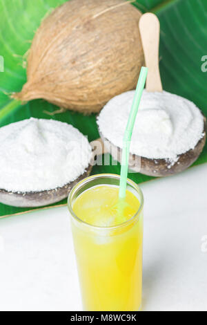 Köstliche vegane Kokos-eis in Schalen auf der Großen Grünen Palm Leaf Glas mit tropischen Fruchtsaft auf weißem Marmor Tisch. Auf Basis pflanzlicher Ernährung Sommer Vac Stockfoto