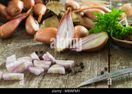 Ganze und gehackte Schalotten Zwiebel auf einem hölzernen Hintergrund mit grüner Petersilie und ein Lorbeerblatt. Geringe Tiefenschärfe. Stockfoto