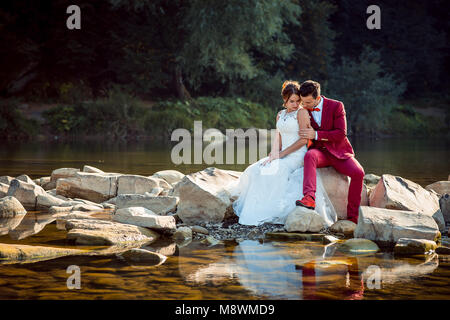 Sensible Jungvermählten liegen in der Nähe des Flusses während umarmen und saß auf dem Stein. Stockfoto