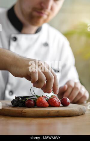 Nahaufnahme eines konzentrierten männlichen Konditors Dekoration Dessert in der Küche Stockfoto