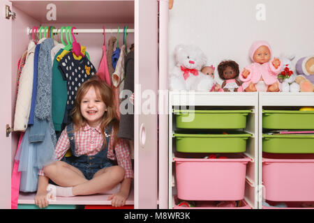 Ein kleines Mädchen sitzt in einem Schrank mit einer Abteilung. Storage System für Sachen und Spielzeug Stockfoto